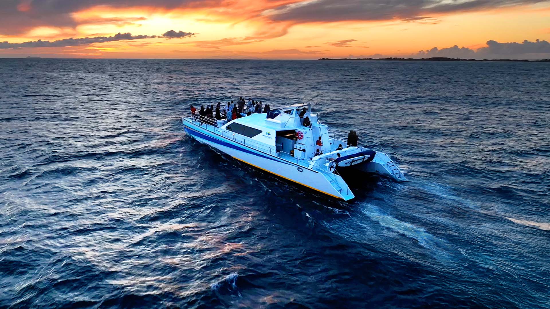 A boat with passengers on ocean at sunset, under colorful sky.